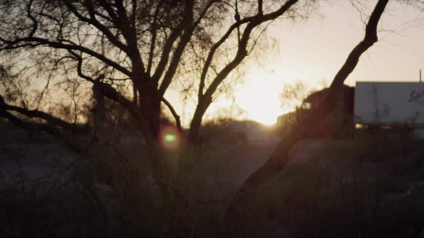A semi truck drives in a rural area at sunset