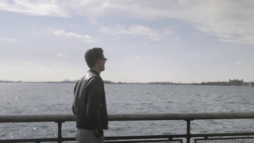 Man walks by a railing in front of water on a sunny day