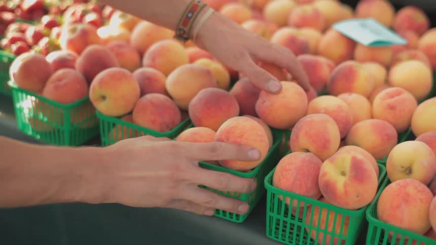 Person placing small bins full of peaches on a table