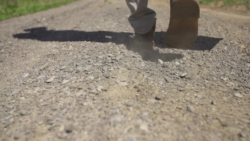A person walks along a dirt and pebble pathway