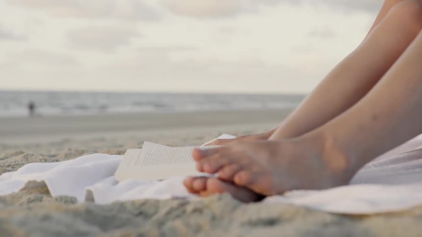 A woman on the beach flips through a book
