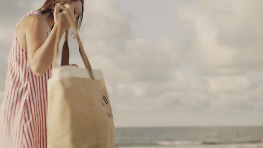 A woman picks up her bag and leaves the beach