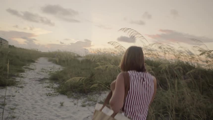 Woman walking on beach trail through tall grass at sunrise