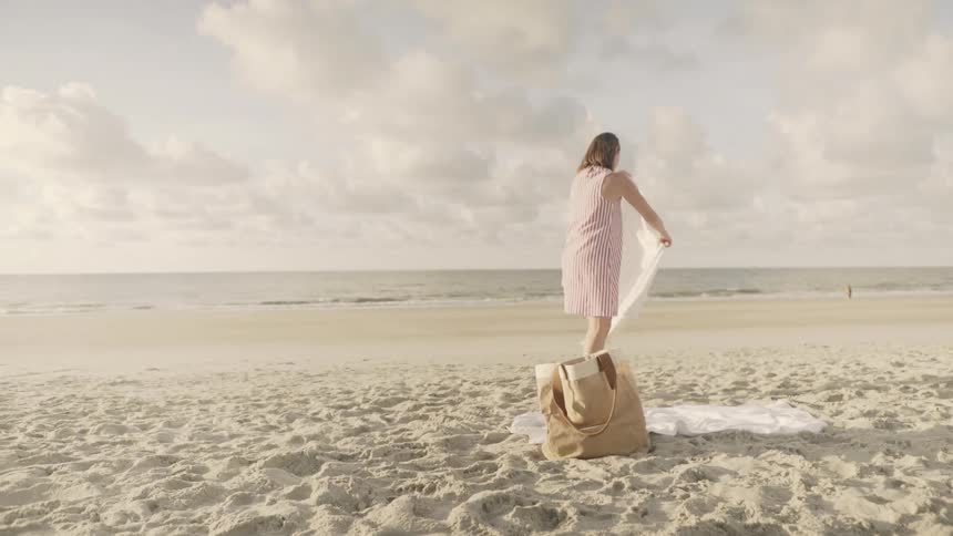 A woman stands up and shakes the sand off a towel on the beach