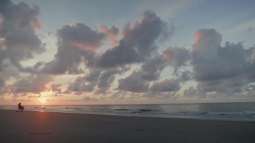 Man Sitting On Beach Fishing At Sunrise