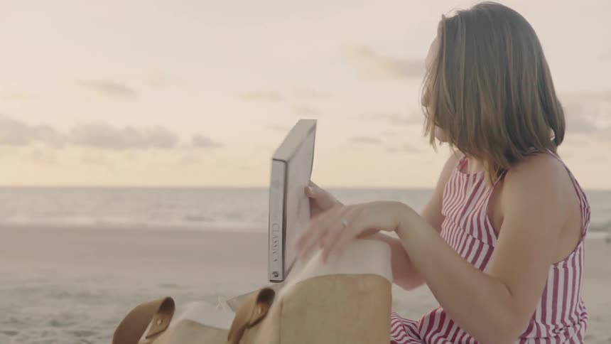 A woman pulls a book from her bag at the beach