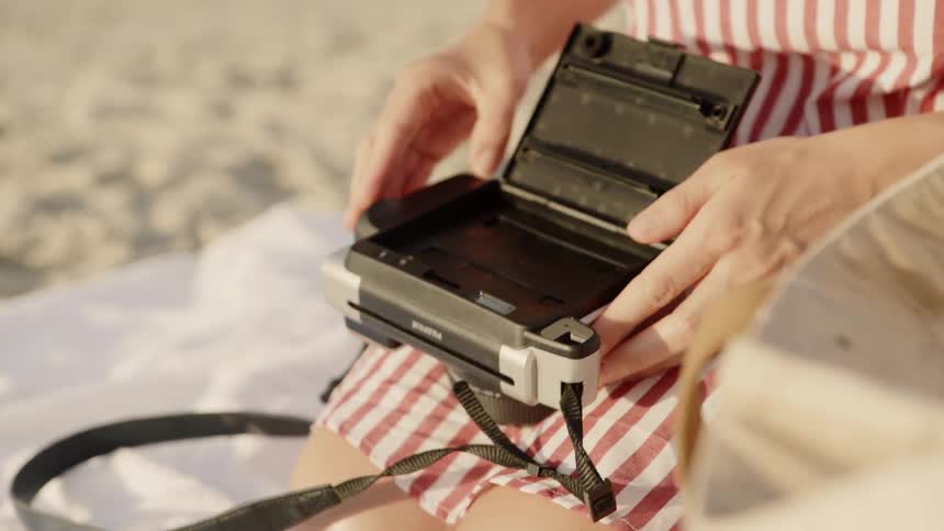 A woman on the beach loads a camera with film