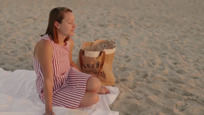 Woman sits on a sandy beach at sunrise