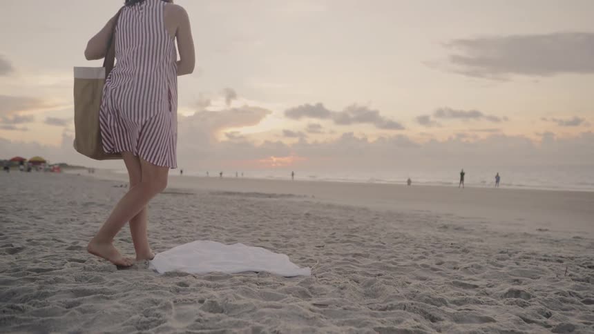 A woman lays a towel down to rest on the beach