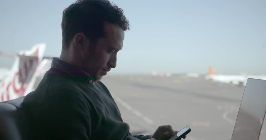 Man scrolls on his phone with a laptop on his lap