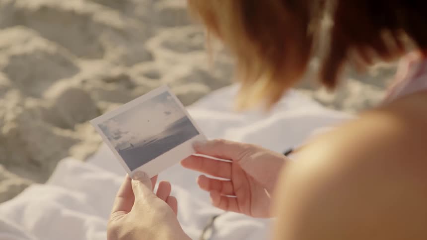 Woman looks at a photograph on a sandy beach