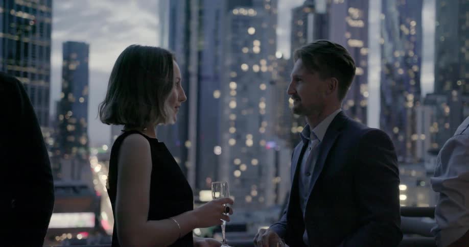 People talk and drink on a balcony overlooking the city