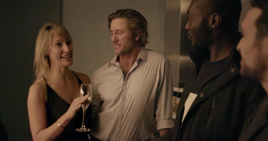 Three men and a woman talk at a party