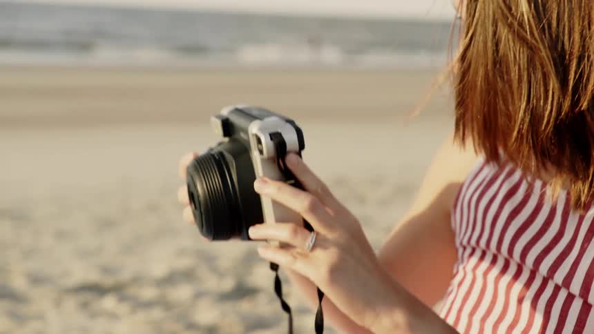 A woman at the beach reaches into her bag and grabs her camera