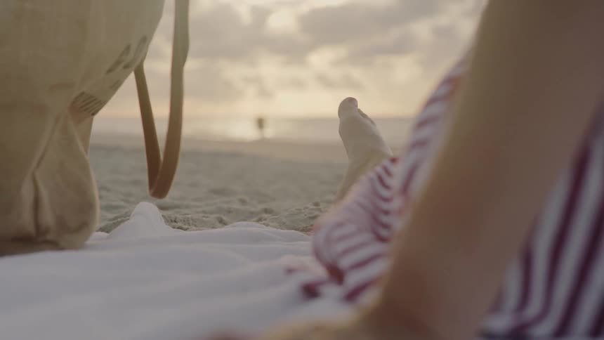 Woman laying on towel on beach at sunset is wiggling her toes