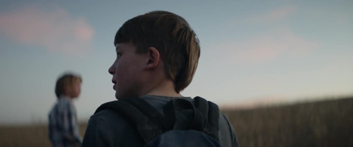 Boys stand in a rural field at sunset