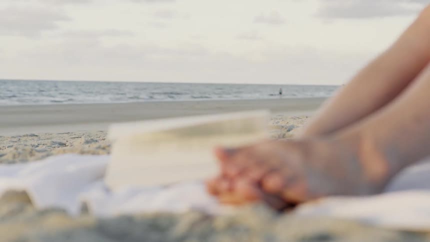 A persons feet are near a book in the sand on a windy day