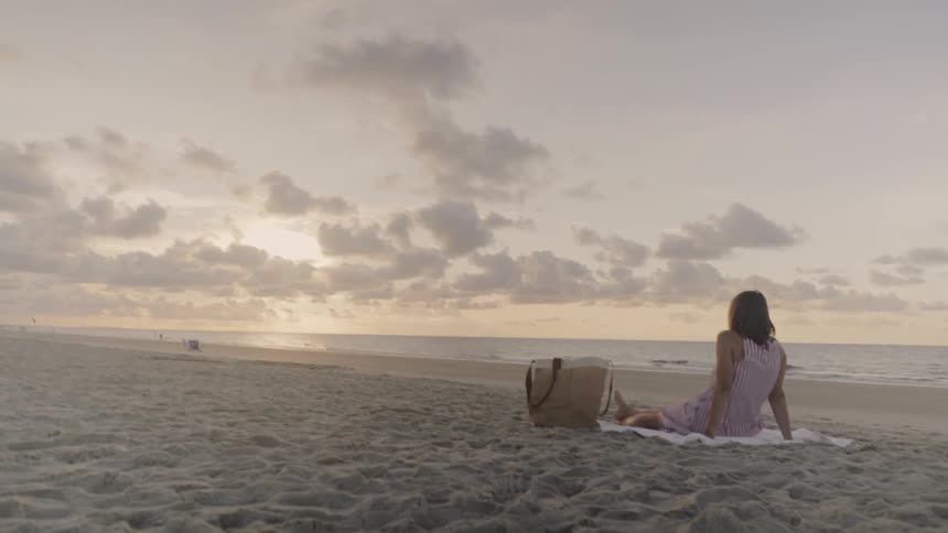 A woman sits on the beach at sunrise