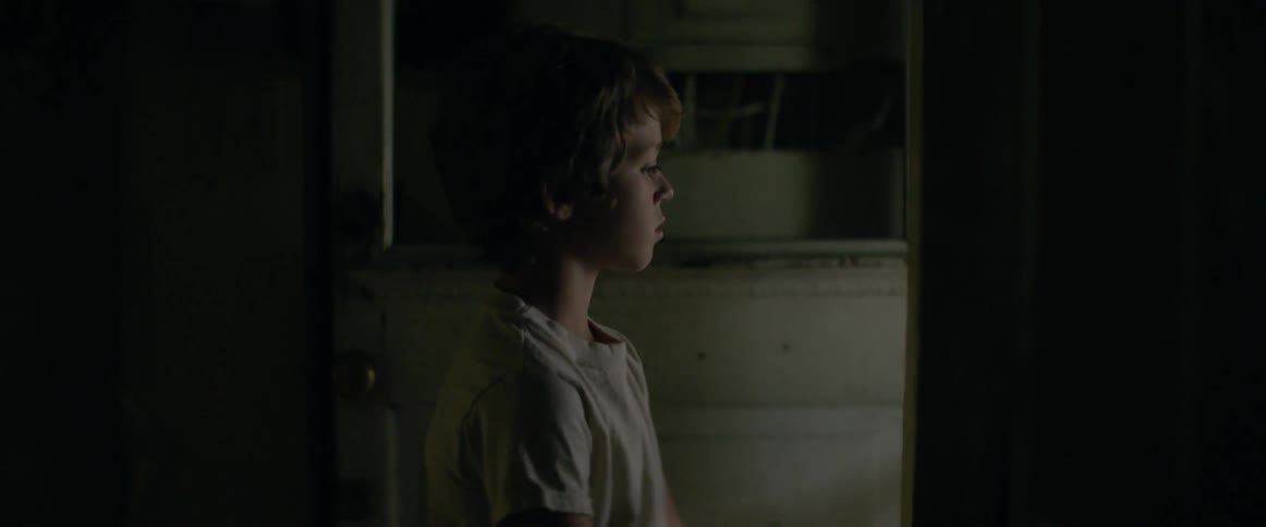 Boy stands in dark room looking out the doorway