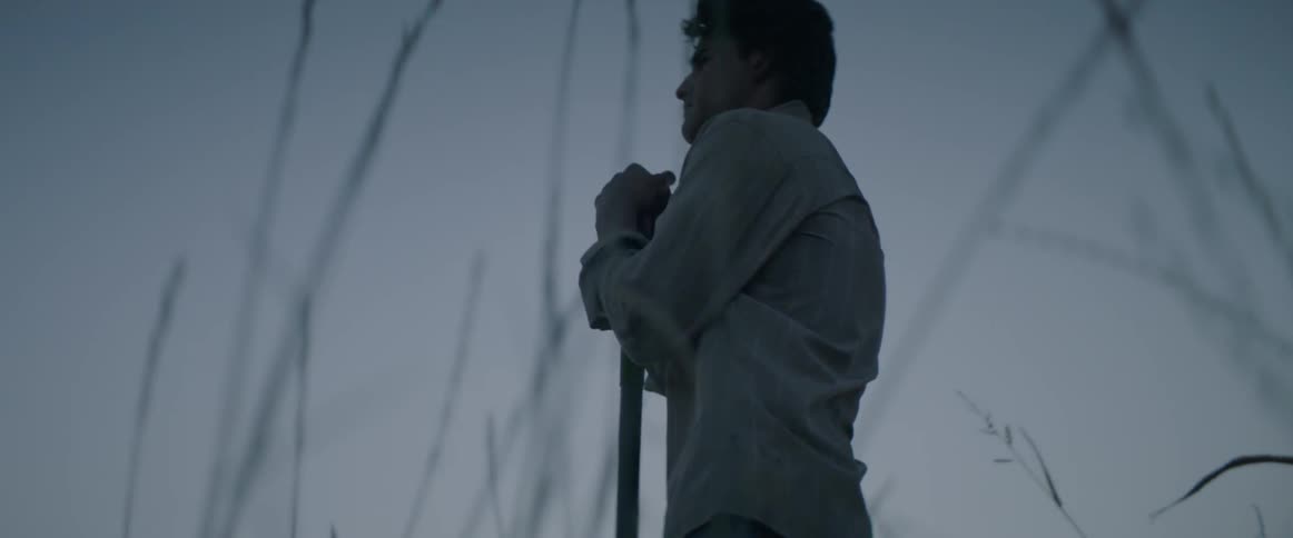 Man stands leaning on a shovel in a field
