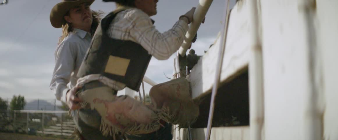 A cowboy helps another jump over the fence in a rodeo