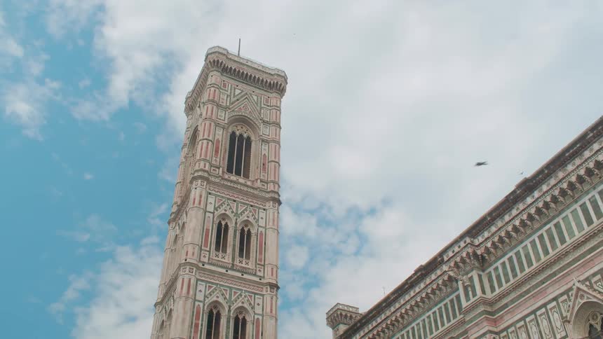 A bird flies past a building on a partly cloudy day
