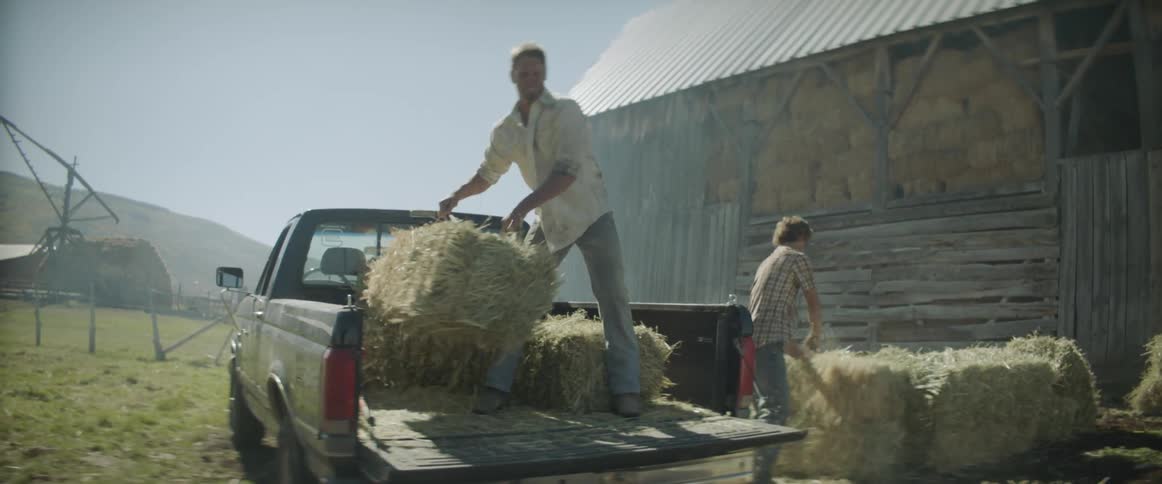 Man lifts bales of hay from a truck and hands them to another man