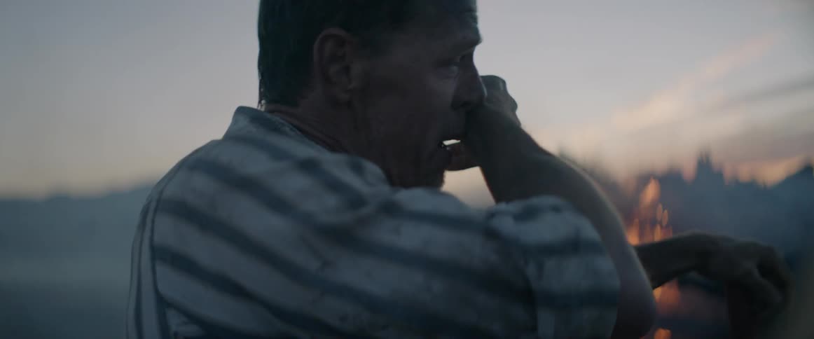 A man wipes the sweat from his face near a fire