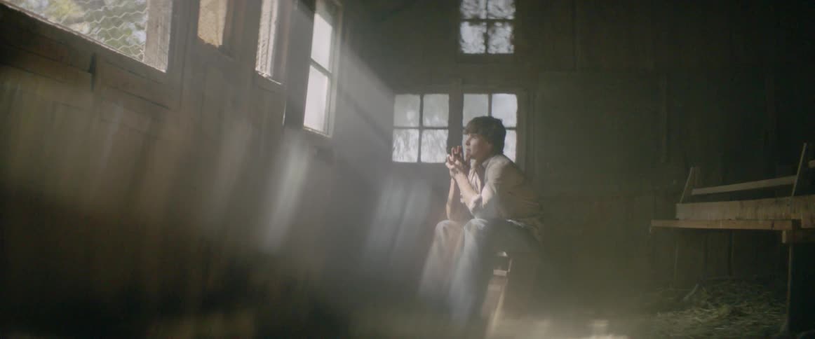 A man is sitting inside a wooden house looking distraught