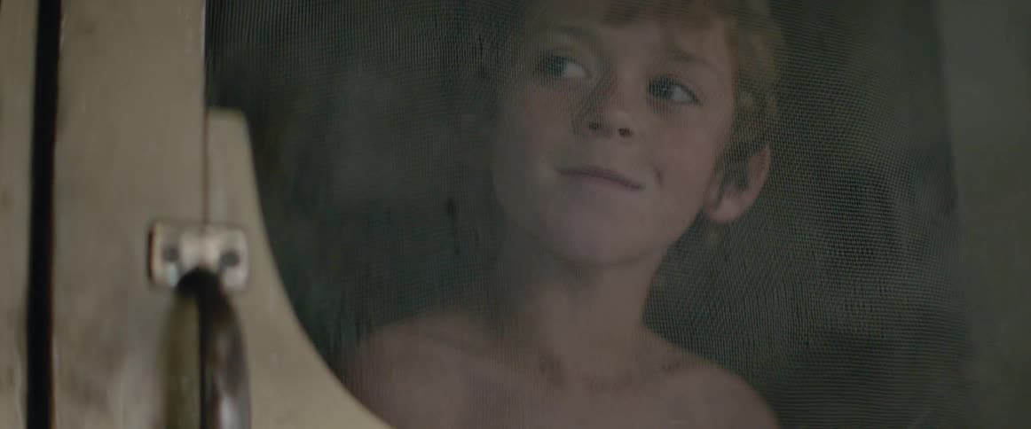 A young boy peers through a screen door, full of quiet optimism