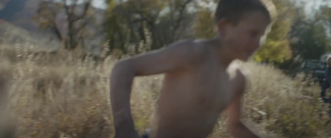 Boys with cowboy hats run through a grassy field