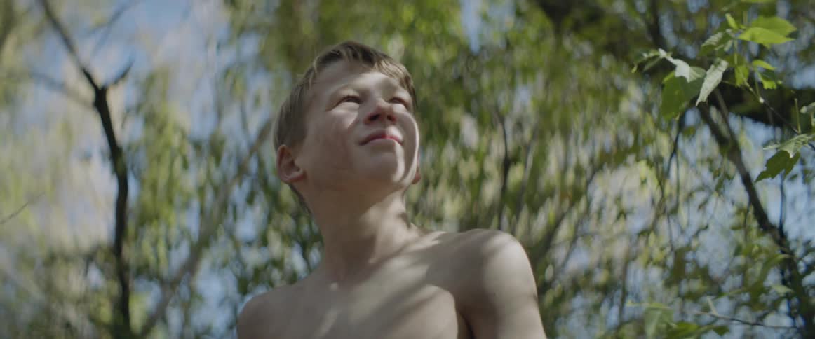 Young boy standing outside under trees is looking back and forth