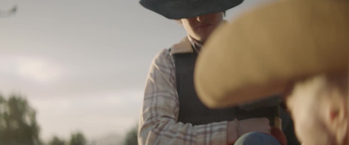 A cowboy sits on a fence at sunset