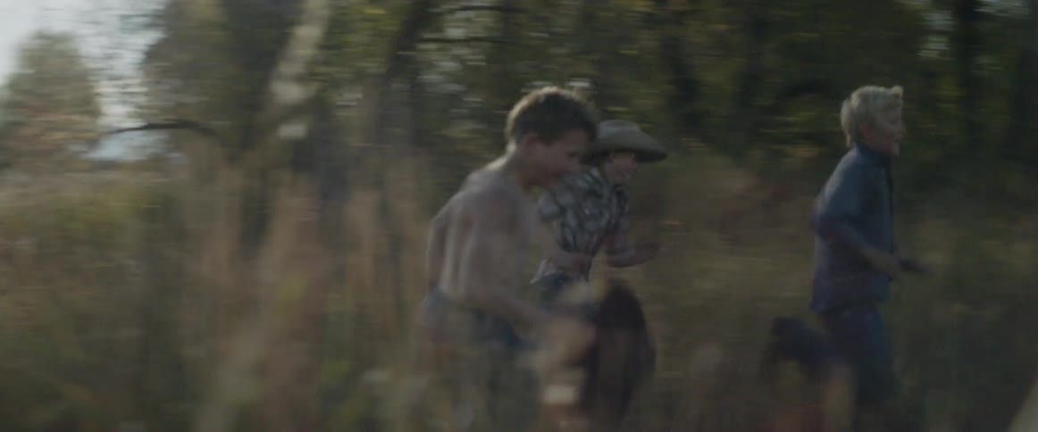 Three boys run through a field on a sunny day
