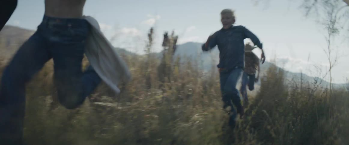 Boys with cowboy hats run through a grassy rural area