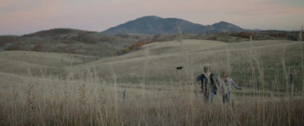 Two children chase each other across the field at sunset