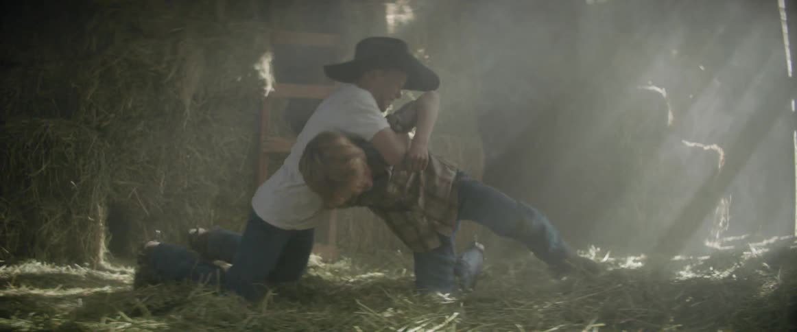 Two kids are wrestling in a barn