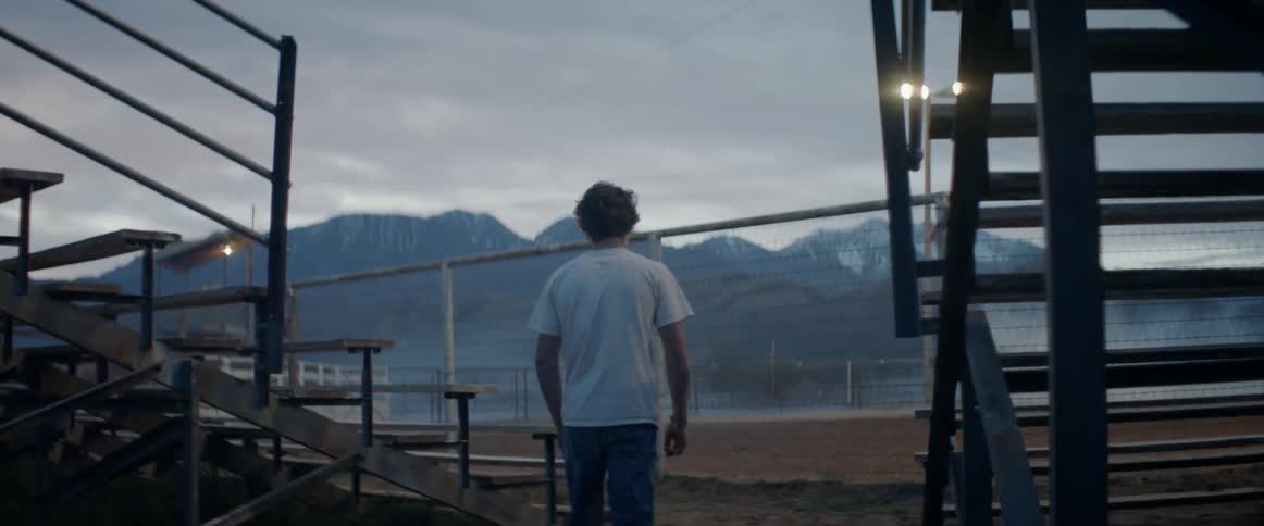 A man walks over to the rodeo ring fence at sunset