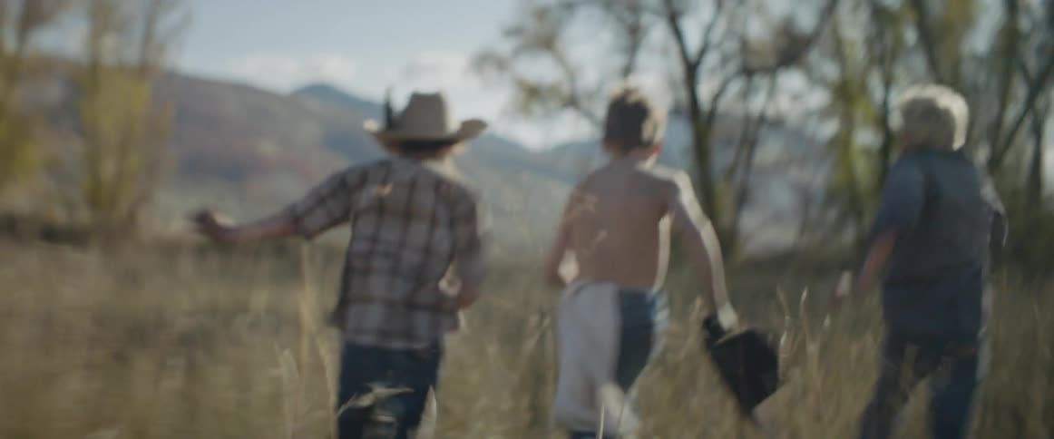 Three children run together down the field towards the trees