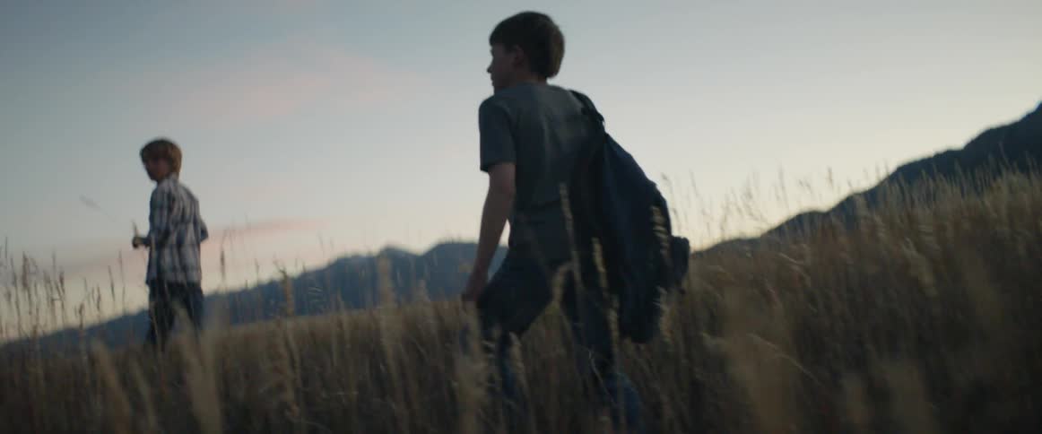 Young boy carries a backpack as he follows another young boy in a field