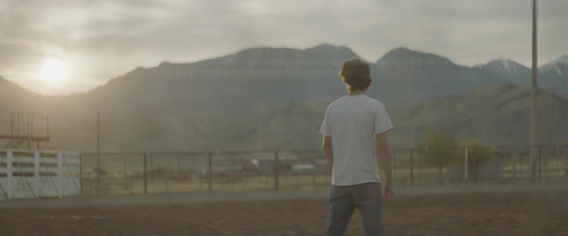 A man is walking in the rodeo ring as the sun sets