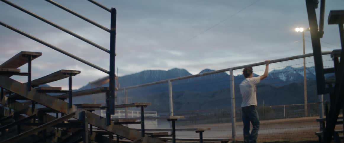 A young man walks towards a fence at a bull riding arena