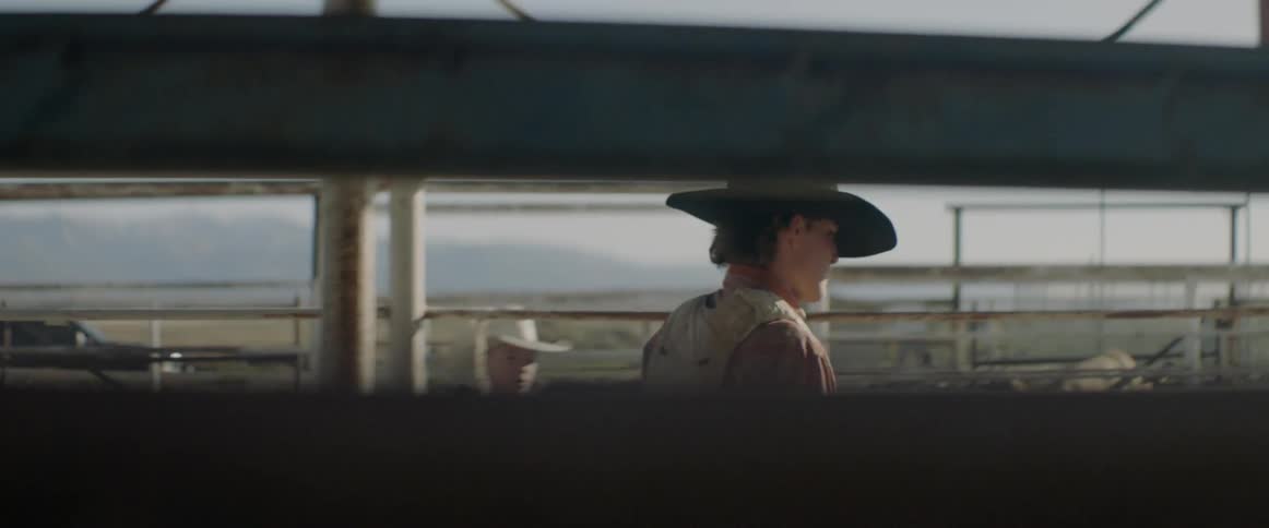 A man in a cowboy hat is climbing up onto a gate