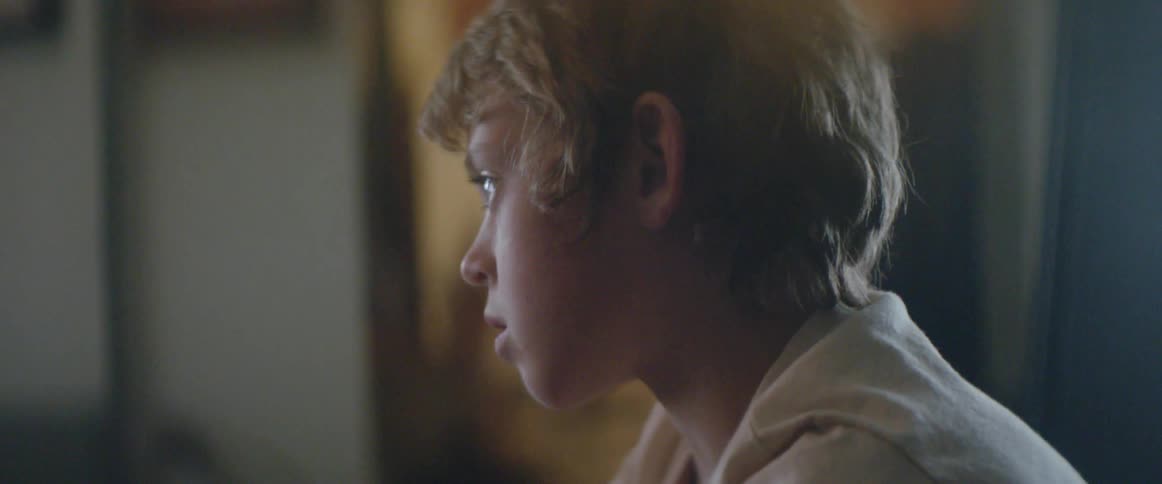 A young boy’s cowboy boots lead up to his focused gaze as he watches television
