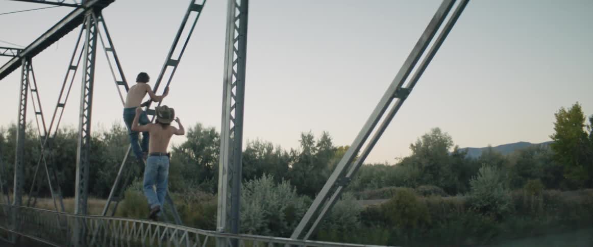 Two cowboys climb on a bridge at dusk