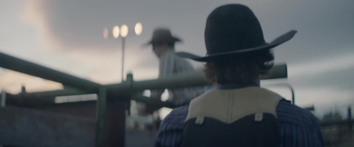 A rodeo rider climbs up on a fence next to cowboys