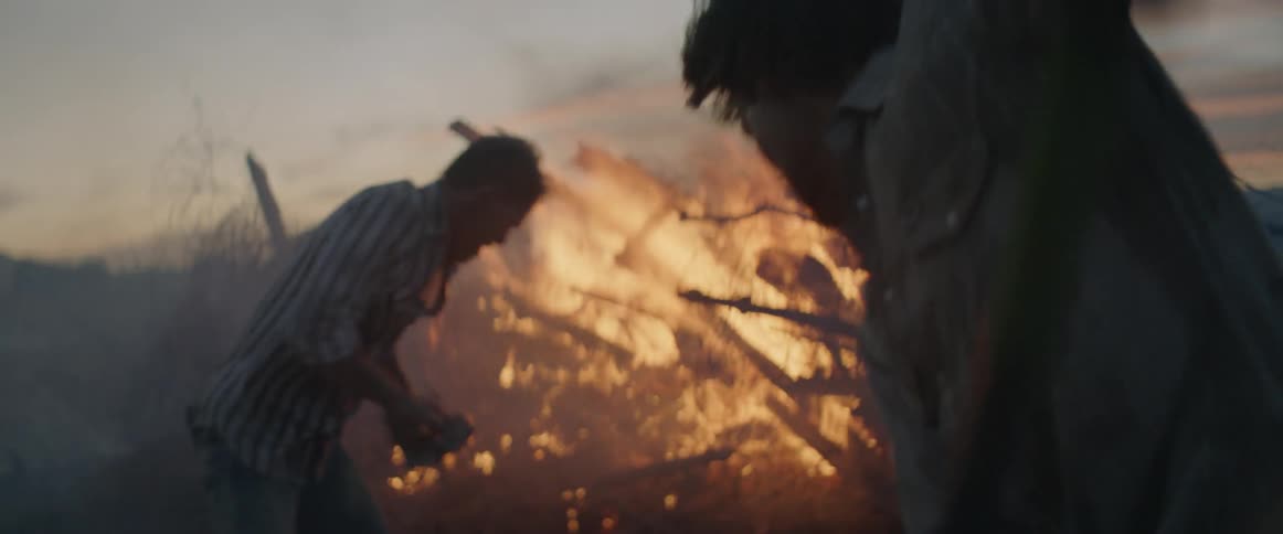 Two people are using shovels to toss dirt onto a fire