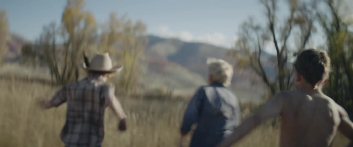 The children run together across the field on a sunny day