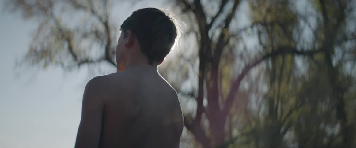 Shirtless boy stands outside on a sunny day