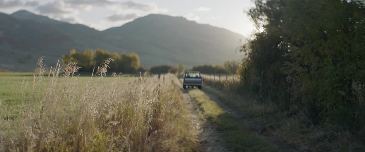 A truck drives down the dirt path towards the mountain